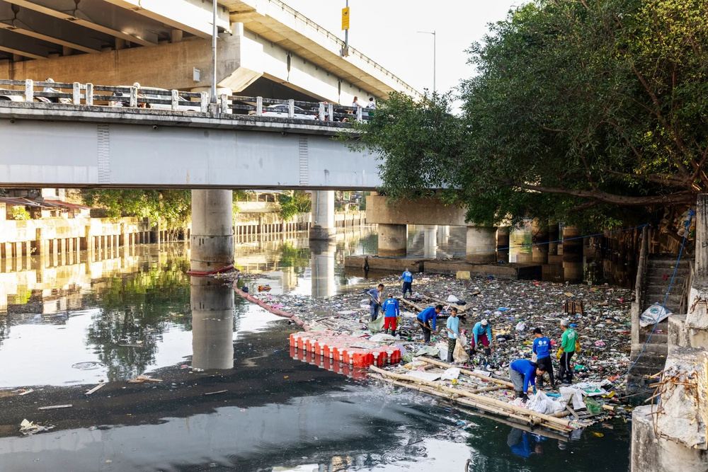 Crew collecting waste from a boom under a bridge in Manila