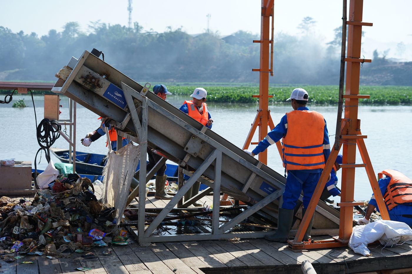 Crew in life vests operating a waste conveyor on a river platform