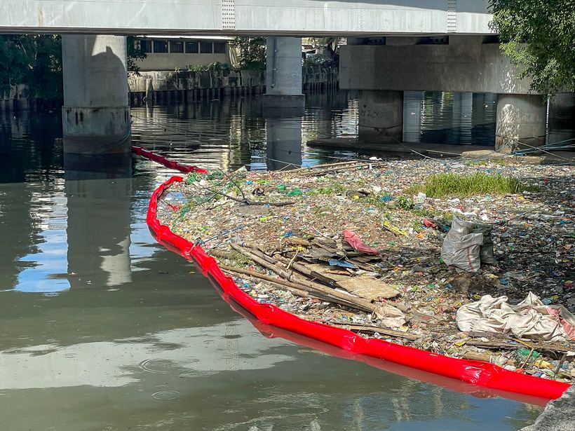 Red floating boom collecting waste under a bridge
