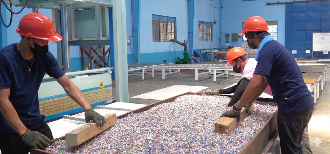 Workers in hard hats spreading shredded plastic in a board mould